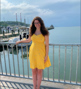 photo of casey nevins, wearing a yellow sundress and standing in front of a marina on a bright sunny day