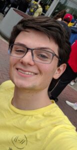 photo of matt gerber, smiling, standing outdoors; he is wearing a yellow t-shirt and glasses