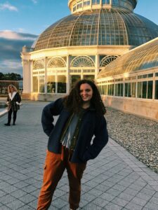 Photo of Nicole Ducret. She has dark curly hair and is standing outside a building with a large glass dome.